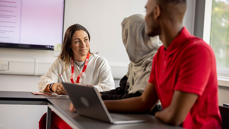 Two students practice for the IELTS speaking section with their teacher